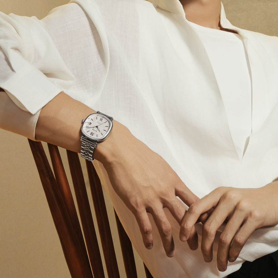 A FIYTA Tempered watch with a light textured dial and silver-tone bracelet worn with a white shirt while seated. (GA850028.WWW)