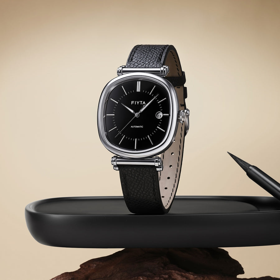 The FIYTA Tempered watch with a black dial and black strap displayed upright on a dark tray beside a pen. (GA850029.WBB)